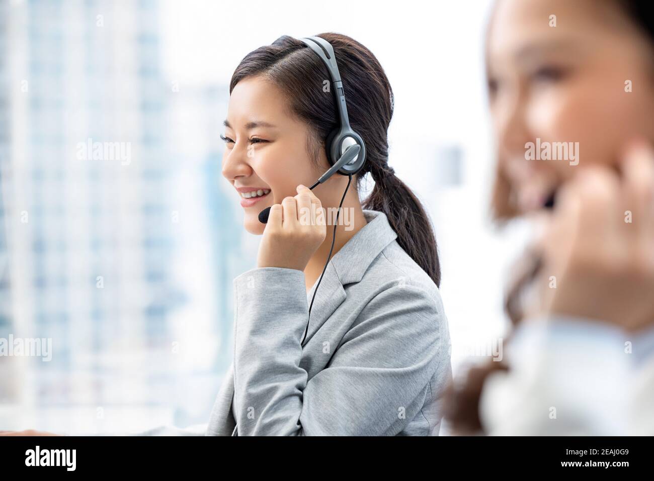 Sorridente bella donna asiatica che lavora nel call center ufficio della città in qualità di operatore del servizio clienti con team Foto Stock