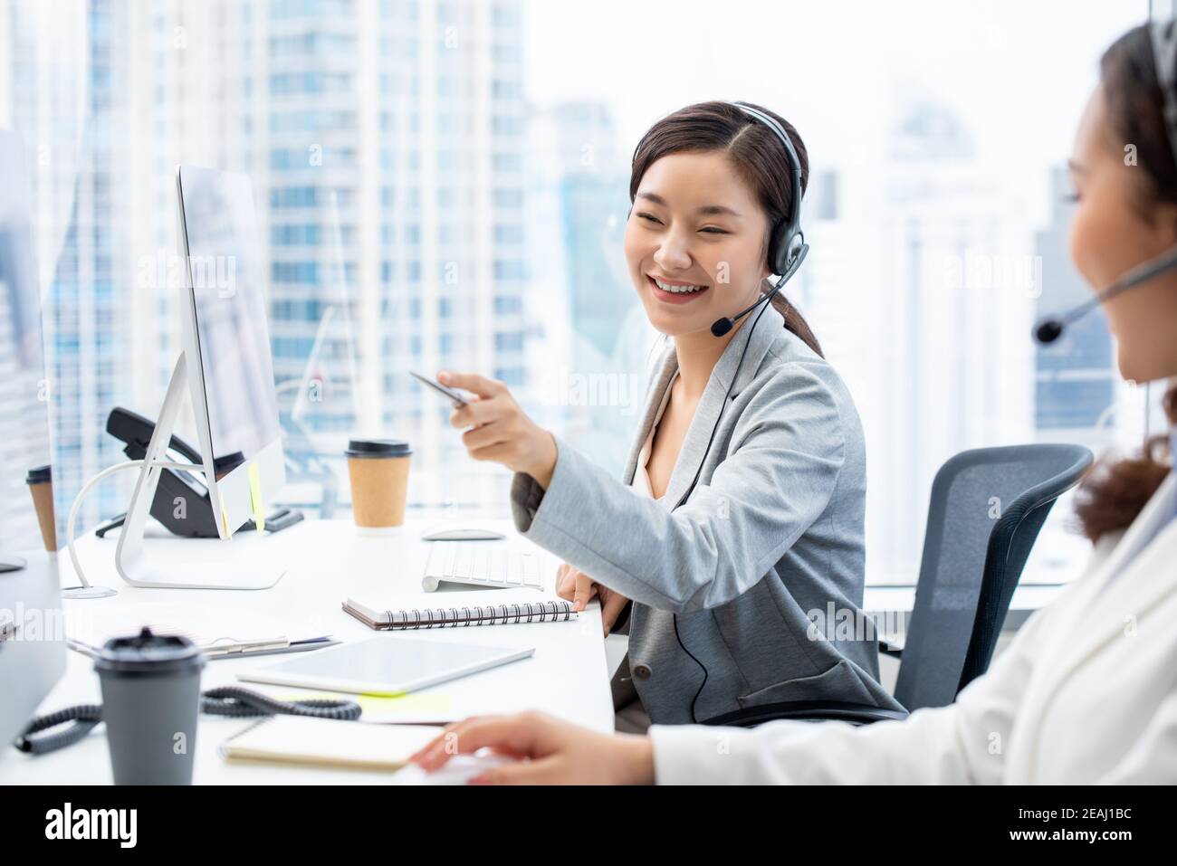 Sorridente bella donna asiatica telemarketing agente di servizio di cliente che lavora dentro ufficio call center con un collega Foto Stock