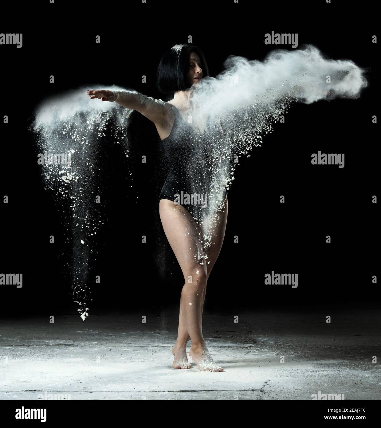 donna con figura atletica che danzano in flying farina bianca sopra sfondo nero Foto Stock