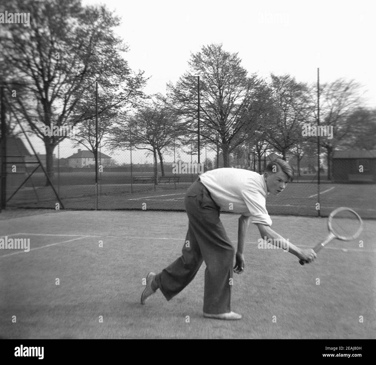 1952, storico, fuori in un parco, un giovane su un campo da tennis con una  racchetta di legno dell'epoca, praticando un volley, Inghilterra, Regno  Unito. Indossare pantaloni lunghi e magliette a manica