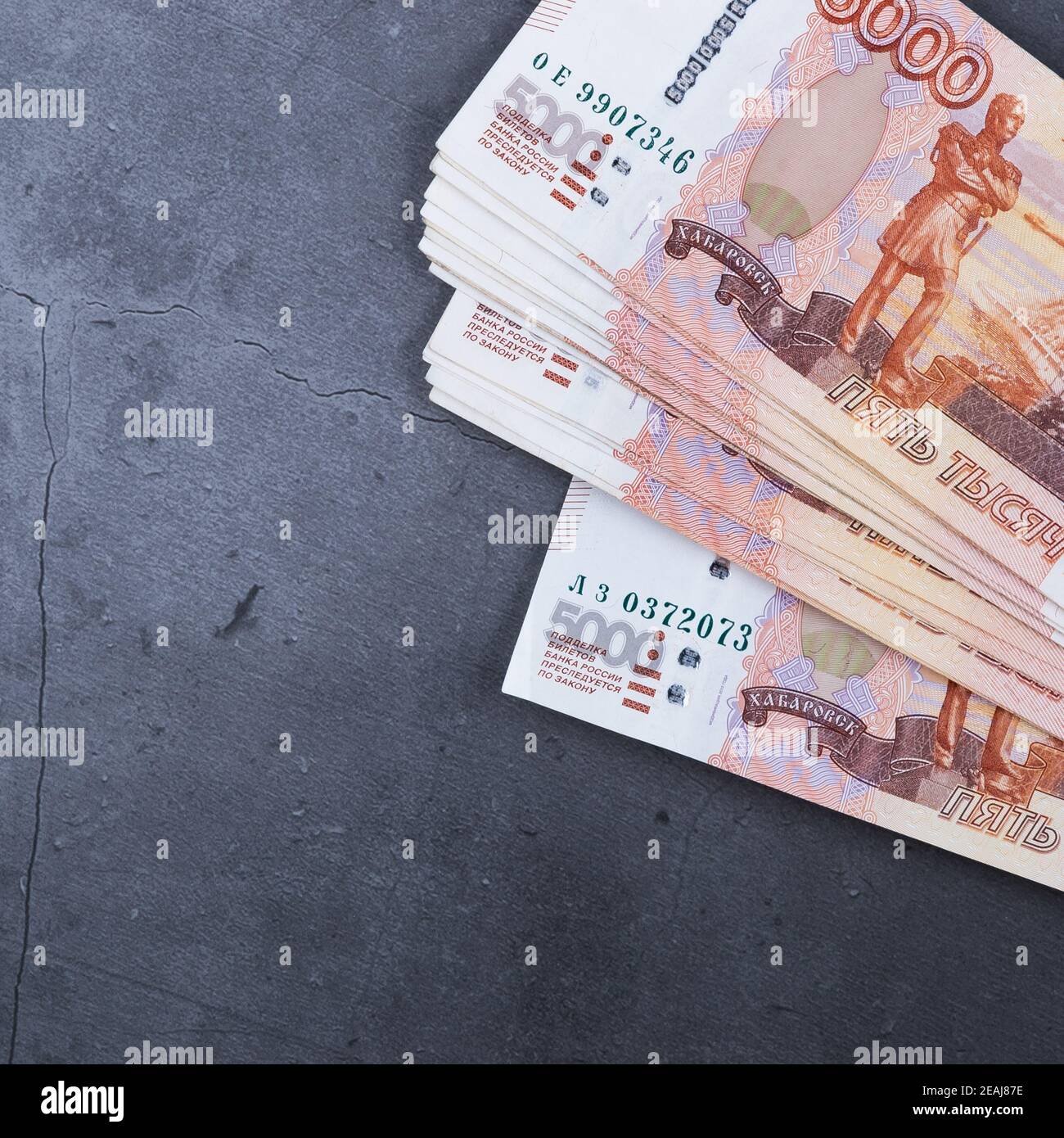 Una grande pila di banconote in denaro russe di cinquemila rubli giacenti su un fondo grigio di cemento. Foto Stock