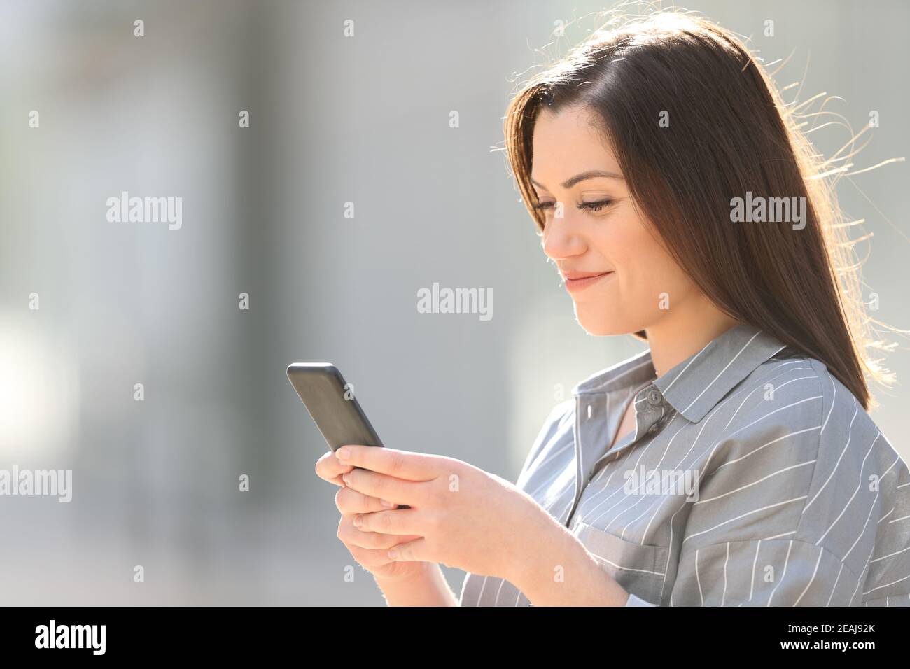 Donna che usa uno smartphone in una strada soleggiata Foto Stock