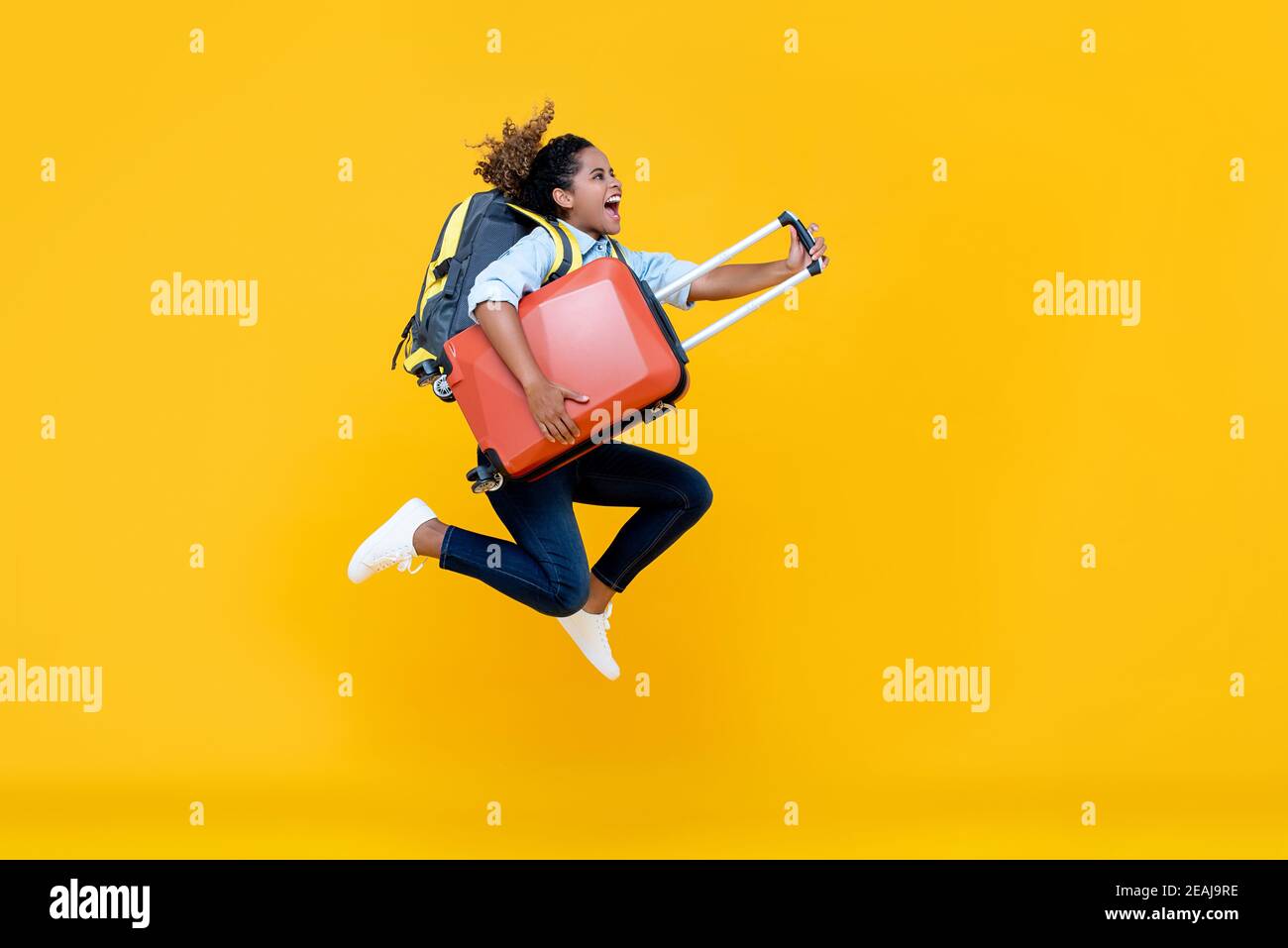 Entusiasta donna turistica afroamericana con zaino e bagaglio salto in studio a mezz'aria girato isolato su colorato sfondo giallo Foto Stock
