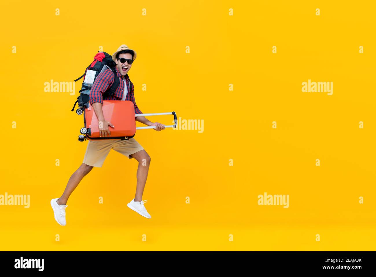Sorridente eccitato bel turista indiano con zaino che tiene il bagaglio e saltando pronto per andare in viaggio isolato su giallo sfondo con copia s Foto Stock