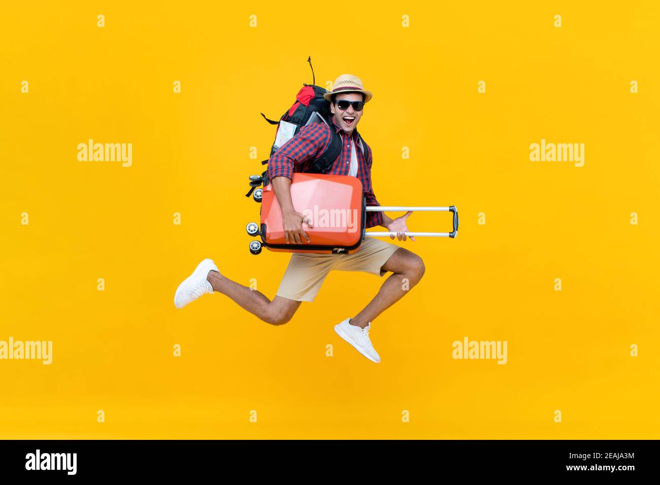 Eccitato giovane turista asiatico con i bagagli saltando isolato su sfondo giallo studio Foto Stock