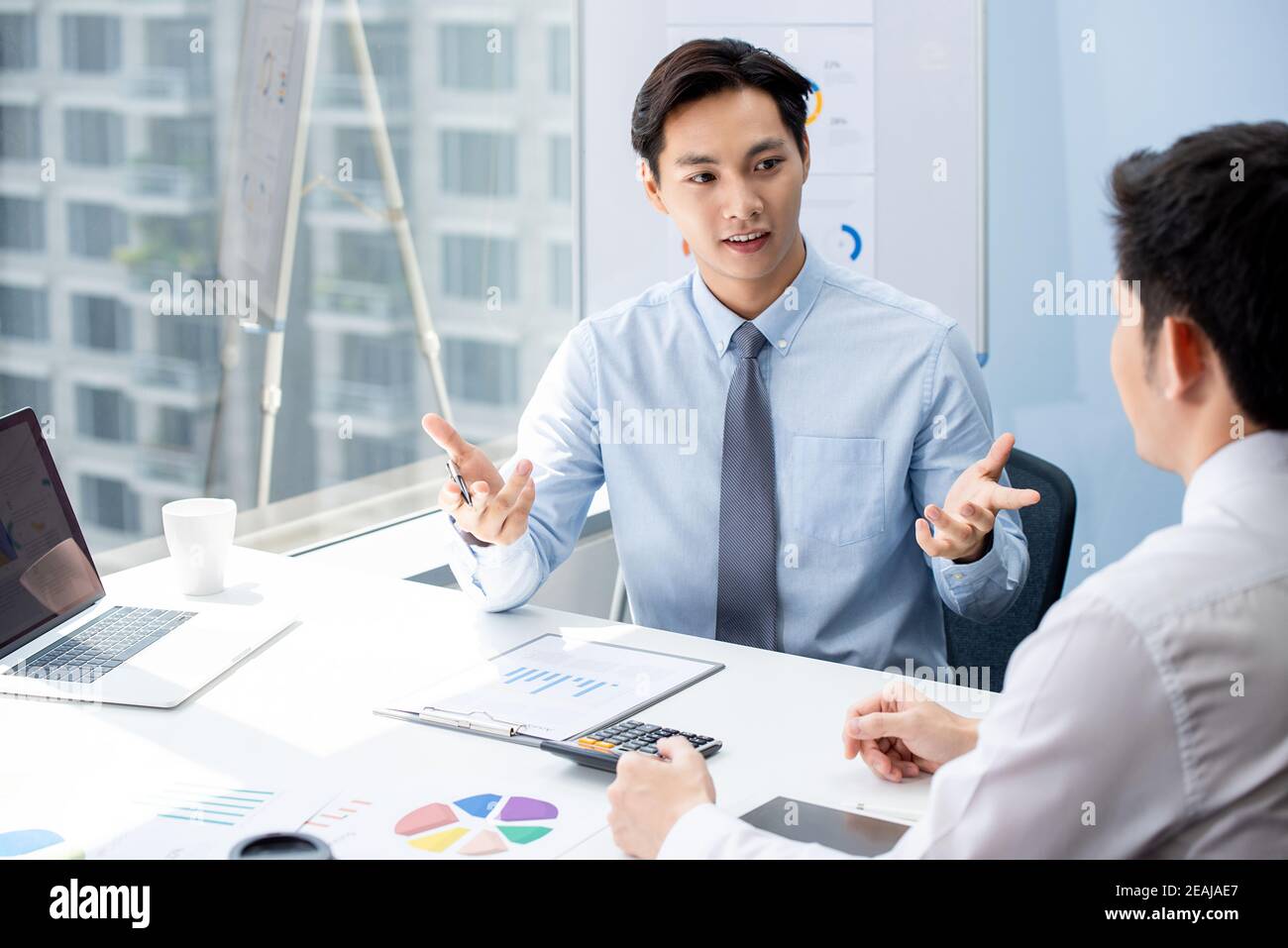 Interessante mediatore finanziario asiatico che esplora i dati aziendali al suo cliente durante la loro riunione privata in ufficio Foto Stock