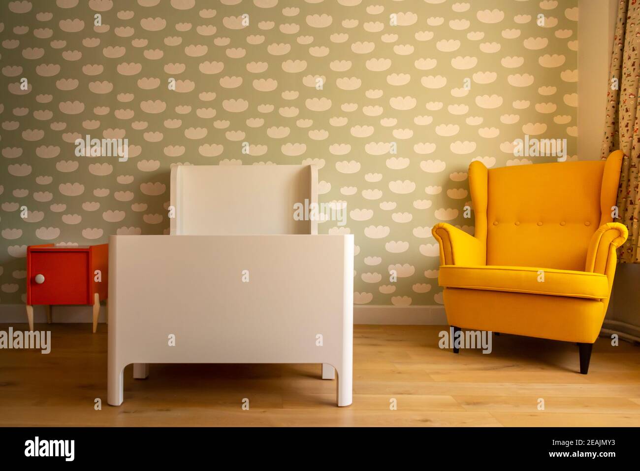 Camera da letto per bambini, con motivi nuvolosi sulla parete, sedia vintage, pavimento in legno e comodino arancione Foto Stock
