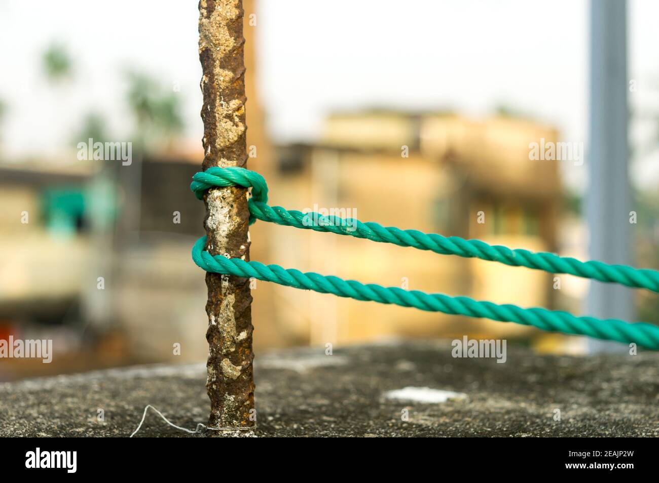Una corda è legata in un nodo intorno a un palo di recinzione, corda legata attacco nodi su un palo di ferro arrugginito isolato da sfondo. Foto Stock