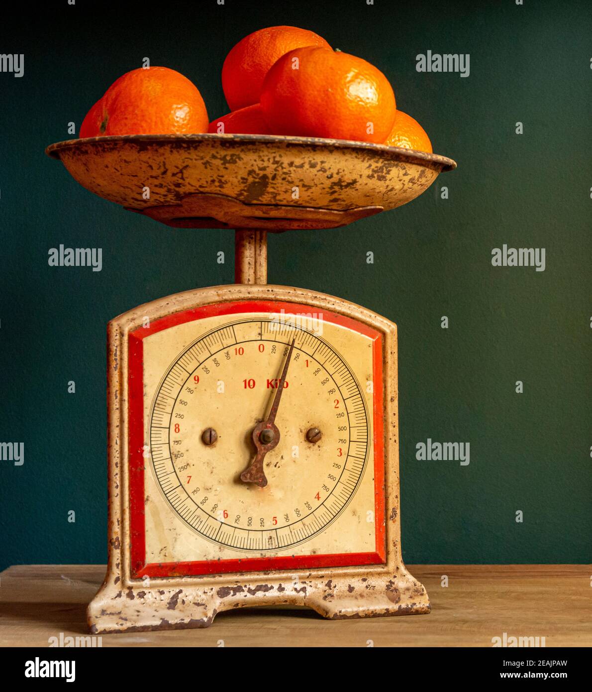 Pesando i tangerini in una scala o in un equilibrio retrò, vintage e usurato, su una tavola di legno contro una parete verde del guatemala. Foto Stock