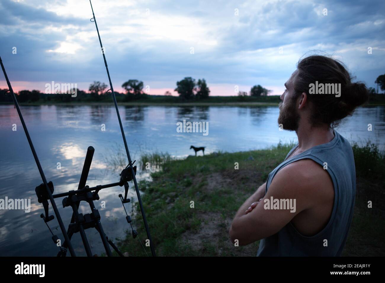 Pescatore in attesa su una riva del fiume al crepuscolo Foto Stock