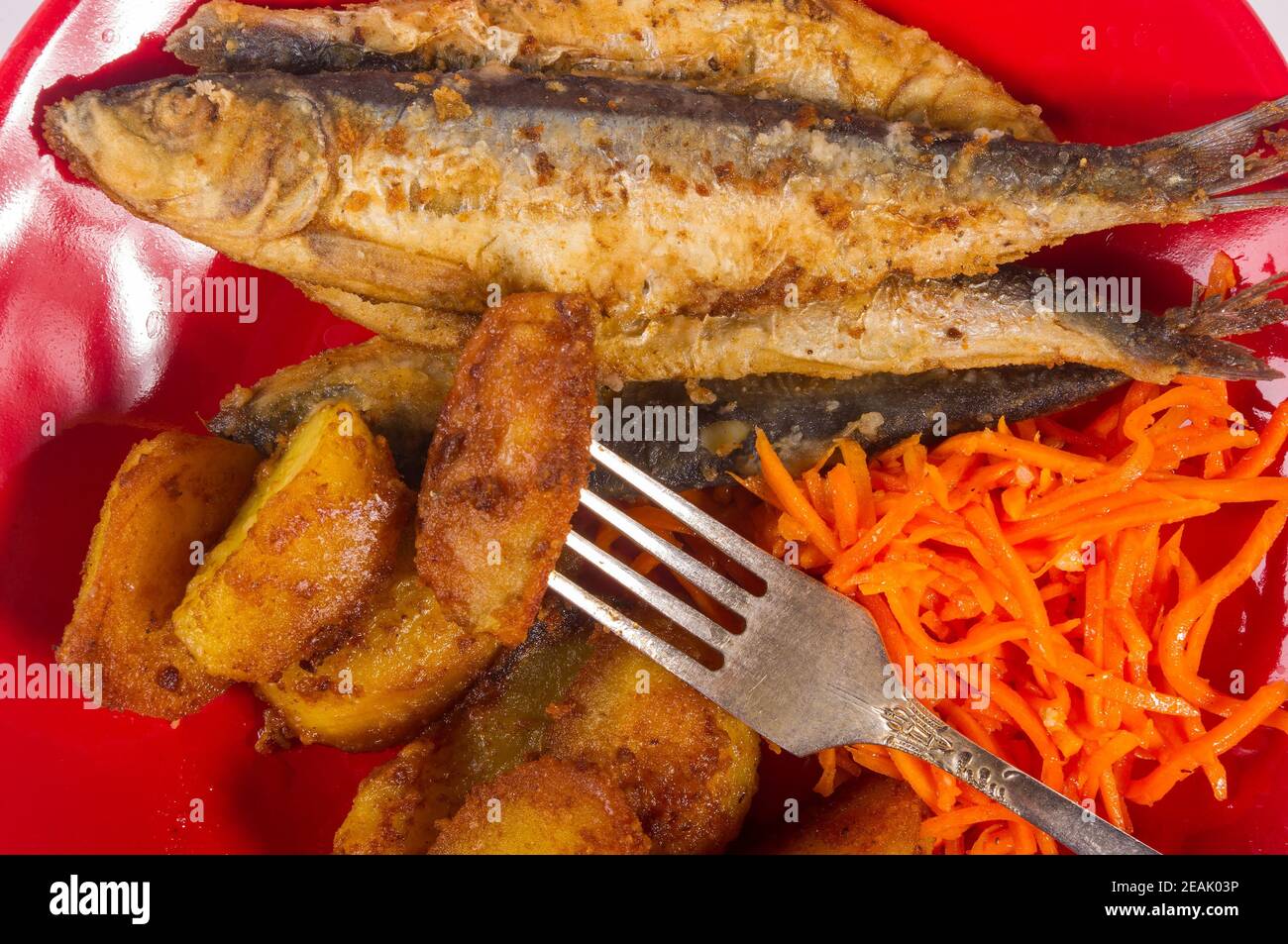 Piatto fatto in casa - spicchi di patate fritte con pesce piccolo e carote  sottaceto su un piatto rosso, semplice cibo rustico, primo piano Foto stock  - Alamy