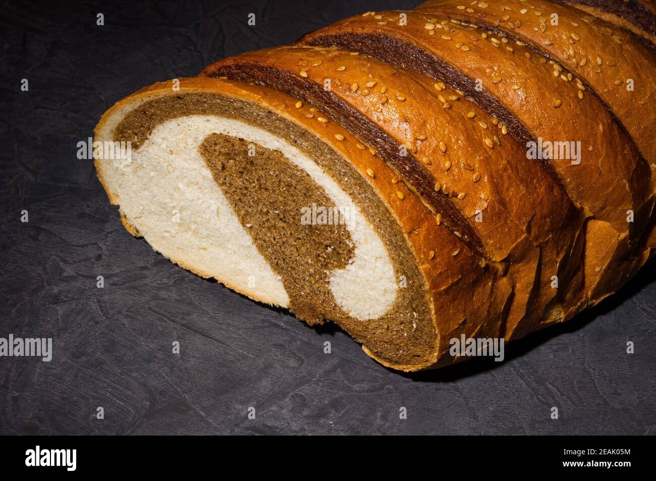 Insolito pane fresco a due colori su sfondo nero, foto in un tasto basso in luce dura, primo piano Foto Stock
