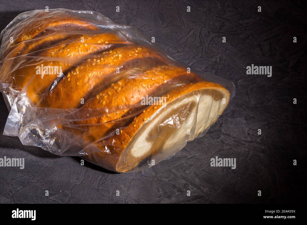 Insolito pane fresco a due colori in una busta di plastica trasparente su sfondo nero, foto in un tasto basso sotto la luce dura, primo piano Foto Stock