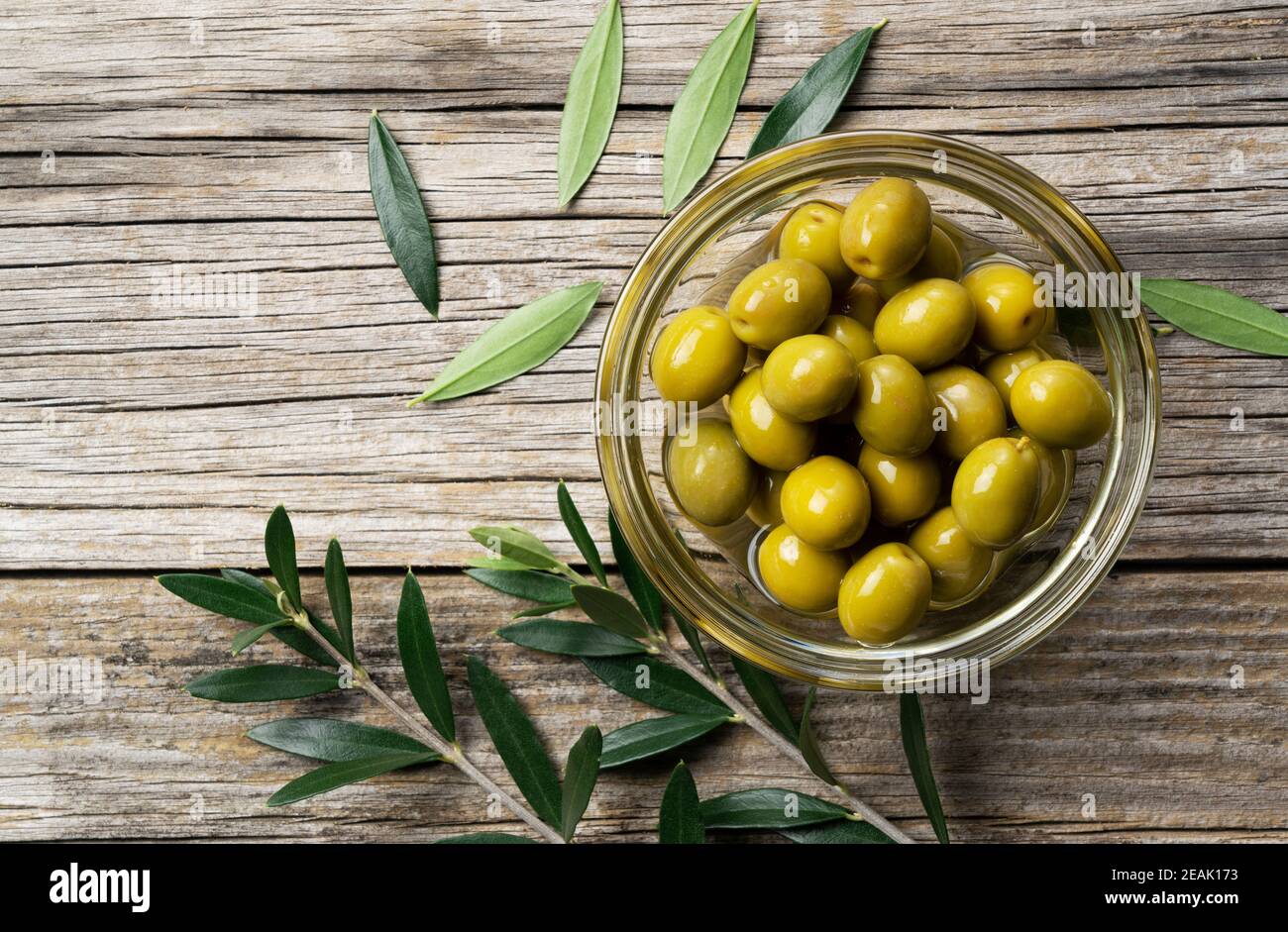 Rami di olive con olive salate poste su uno sfondo di vecchie tavole di legno Foto Stock