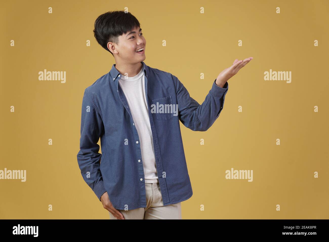ritratto di felice eccitato bel giovane asiatico vestito casualmente sorridente con gesto a mano aperta isolato su sfondo giallo dello studio Foto Stock