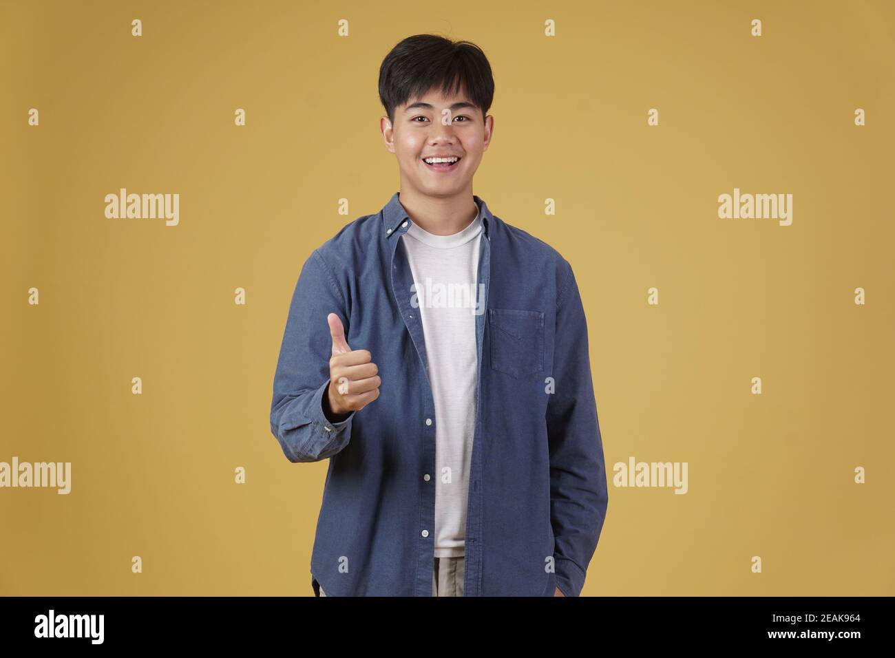 ritratto di sorridente positivo giovane asiatico vestito casualmente movimento thumb up che approva l'espressione isolata su sfondo giallo dello studio Foto Stock
