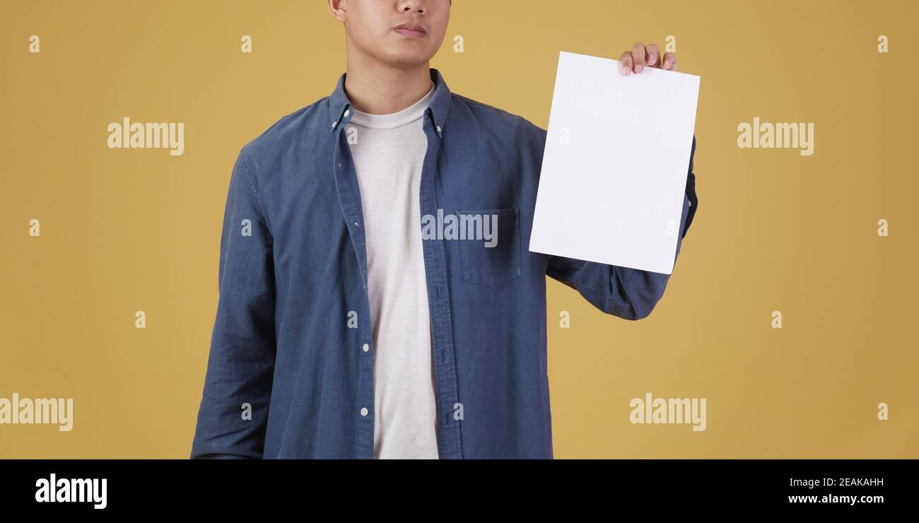 ritratto di giovane asiatico vestito casualmente mostrando carta vuota vuota placard isolato su sfondo giallo studio. Foto Stock