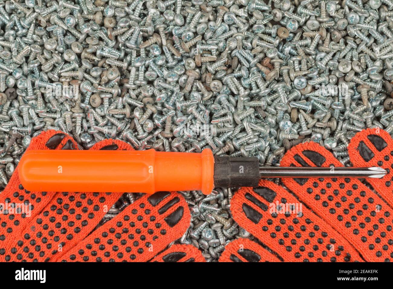 Il cacciavite e i guanti da lavoro giacciono su una pila di viti. Foto Stock