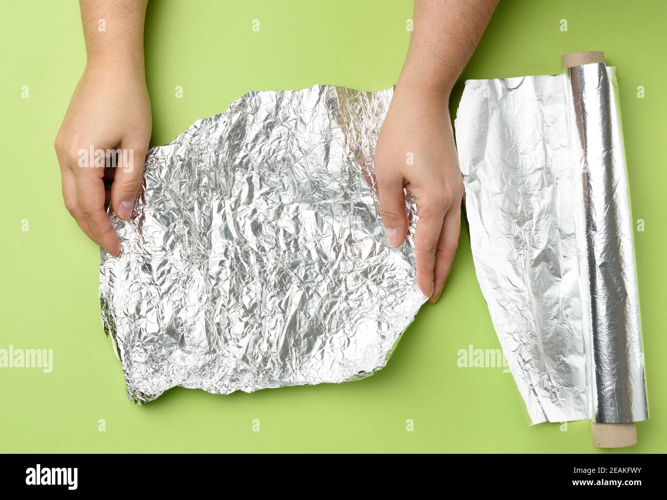 due mani femminili trattengono il foglio d'argento sminuzzato su un verde sfondo Foto Stock