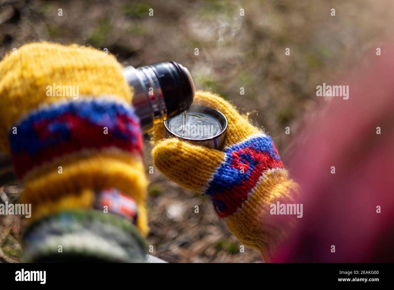 Mani in mittens colorati che versano una bevanda calda da thermos Foto Stock
