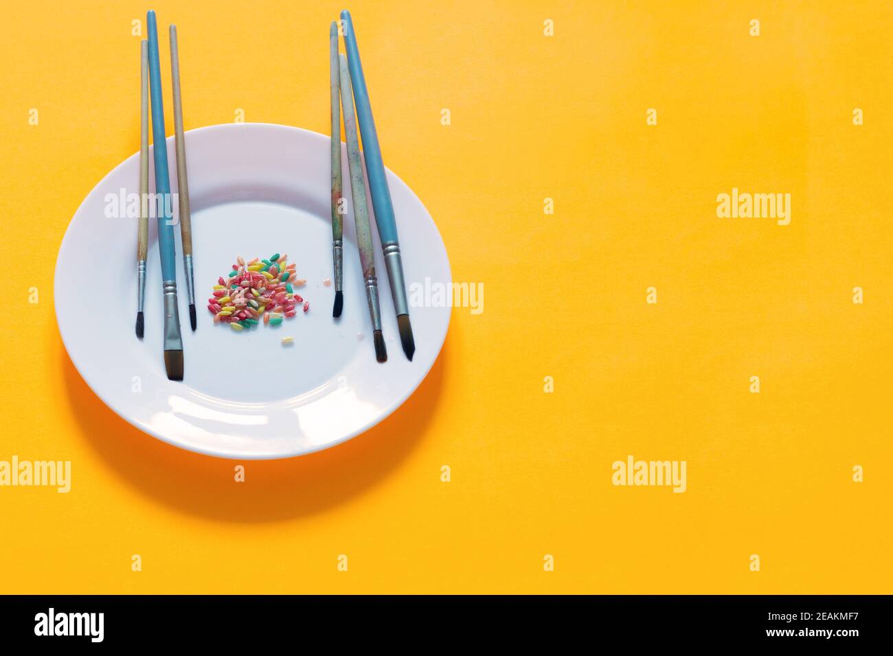 Spazzole e riso dipinte in diversi colori su un piatto, sfondo giallo Foto Stock