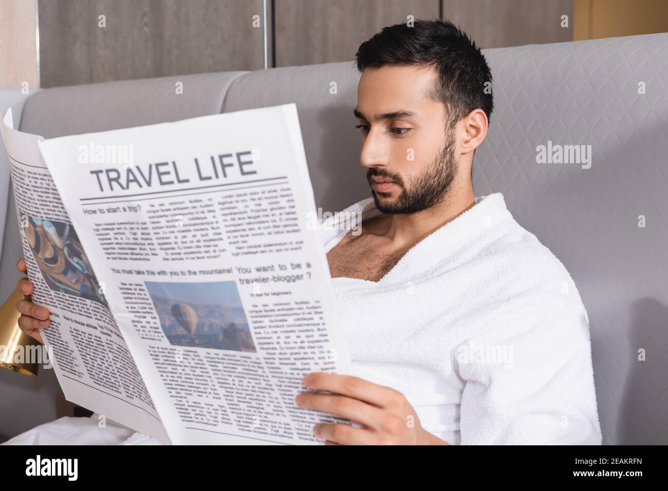 Uomo arabo che legge giornale con vita di viaggio su primo piano sfocato in hotel Foto Stock