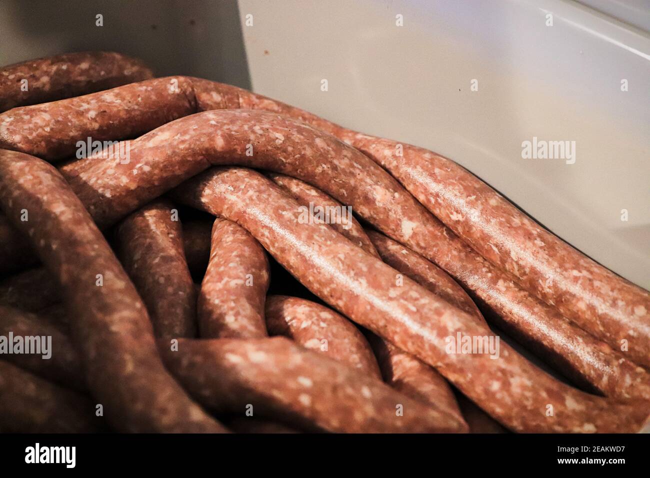 Primo piano di salsiccia cruda in involucri riposanti in una vasca Foto Stock