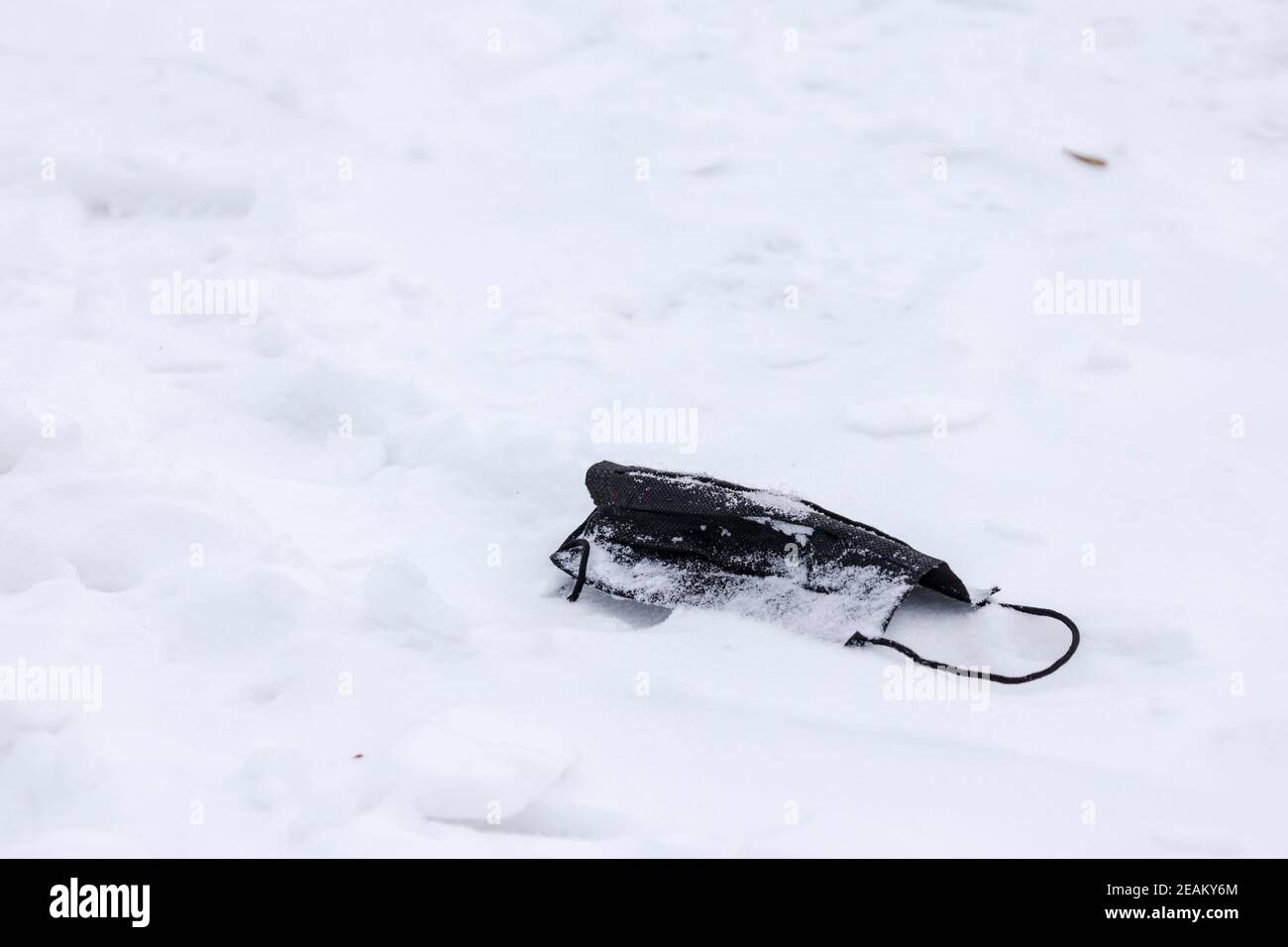 Maschera monouso caduto nella neve. Maschera nera di protezione dal virus corona gettata via durante gli sport invernali. Foto Stock