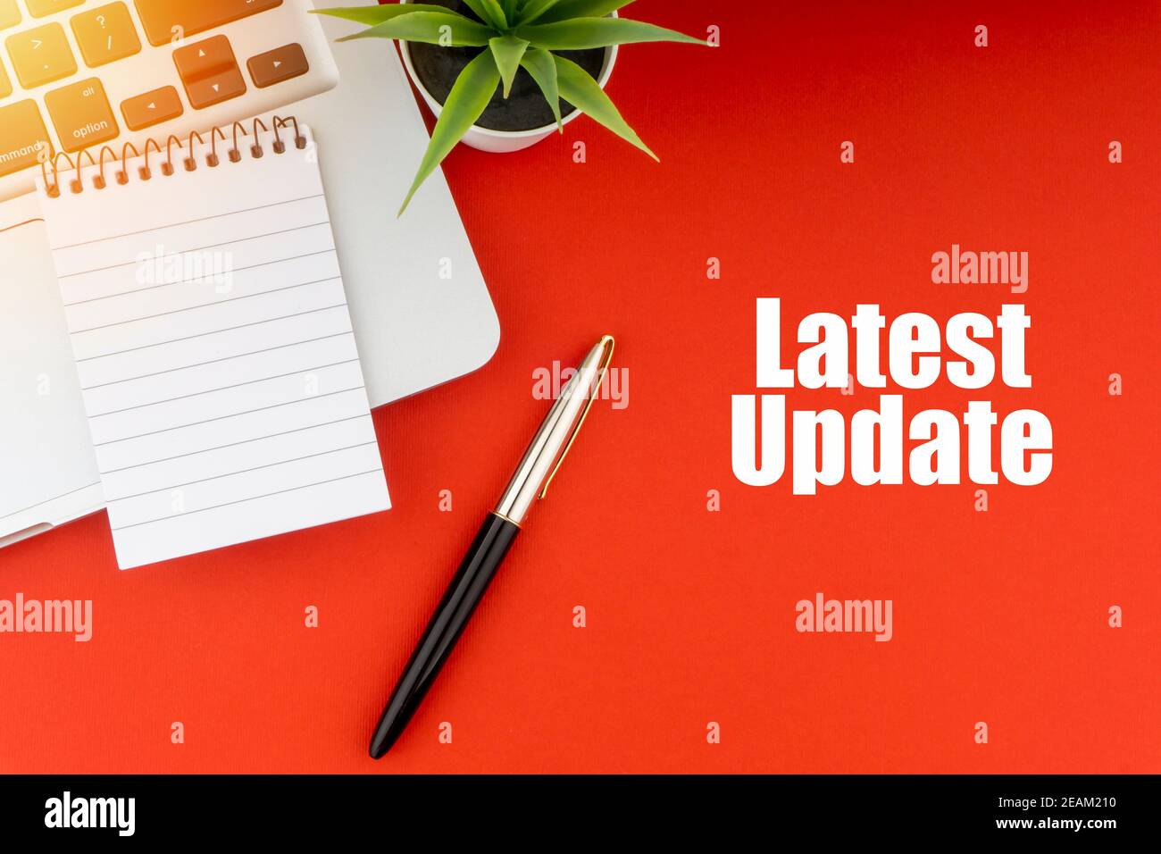 ULTIMO AGGIORNAMENTO testo con blocco note, laptop, penna stilografica e pianta decorativa su sfondo rosso. Foto Stock