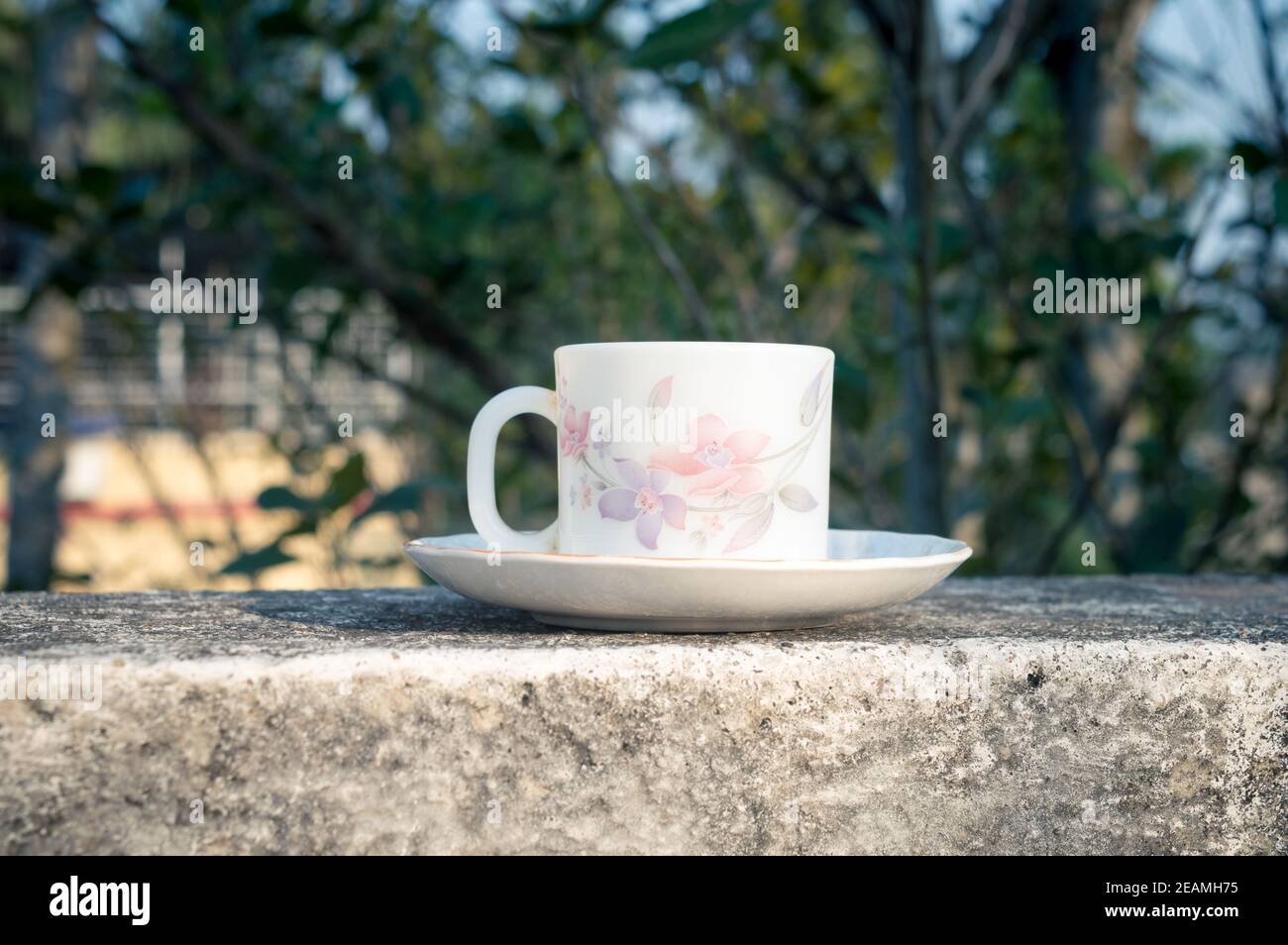 Tazza di caffè alla luce del sole del mattino. Look fresco estivo. Tazza di caffè bianca sul piattino per bevande calde sul tetto di un edificio residenziale con sfondo bokeh. Foto Stock