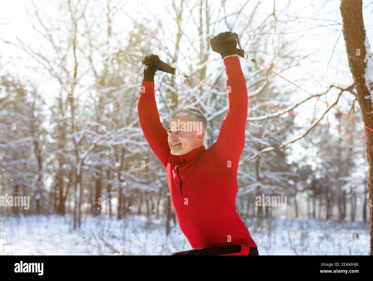 Formazione funzionale all'aperto. Uomo maturo che utilizza cinghie di sospensione per esercitare i muscoli superiori del corpo in un parco invernale innevato Foto Stock
