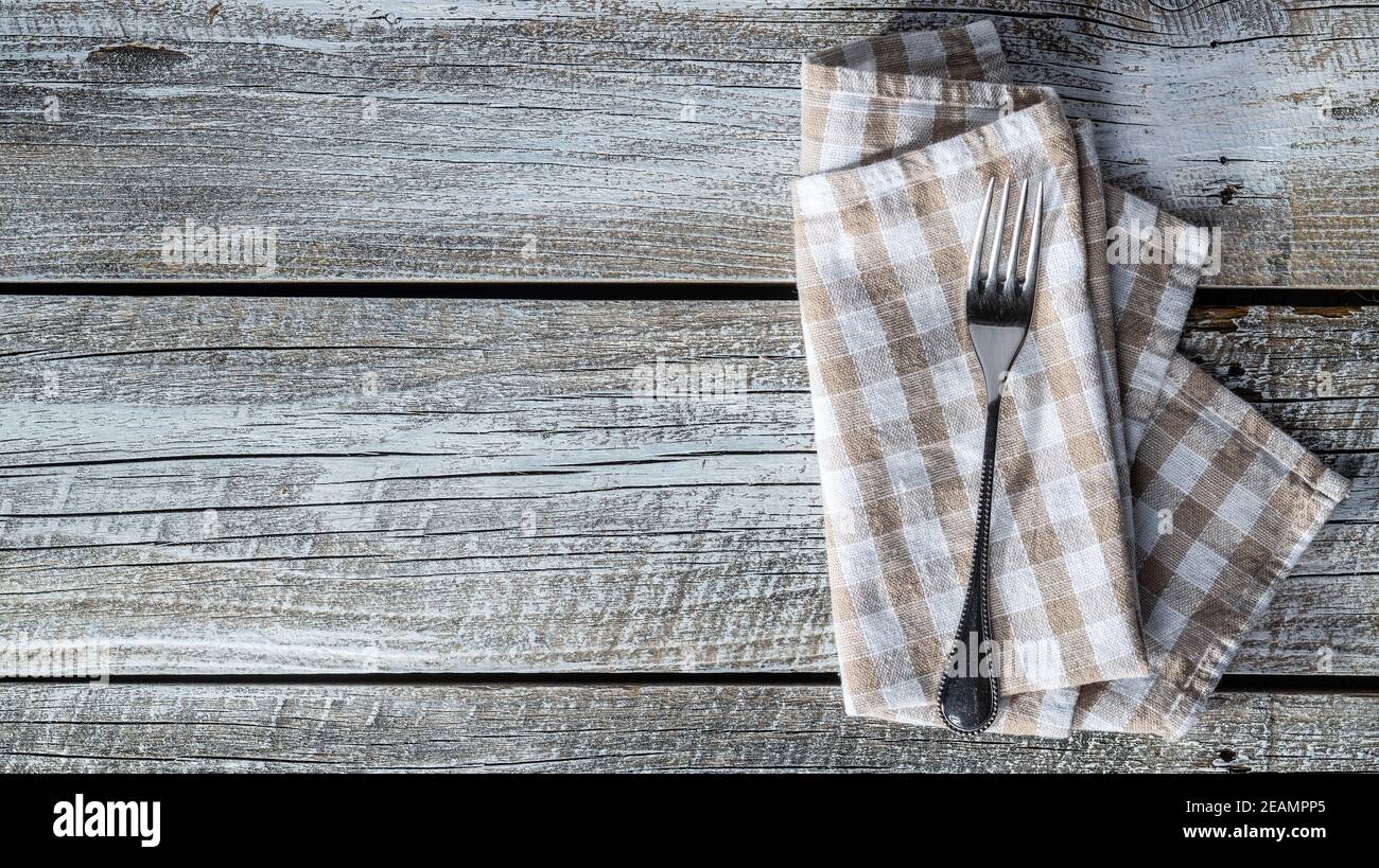 Forchetta e tovagliolo a scacchi su tavolo di legno. Foto Stock