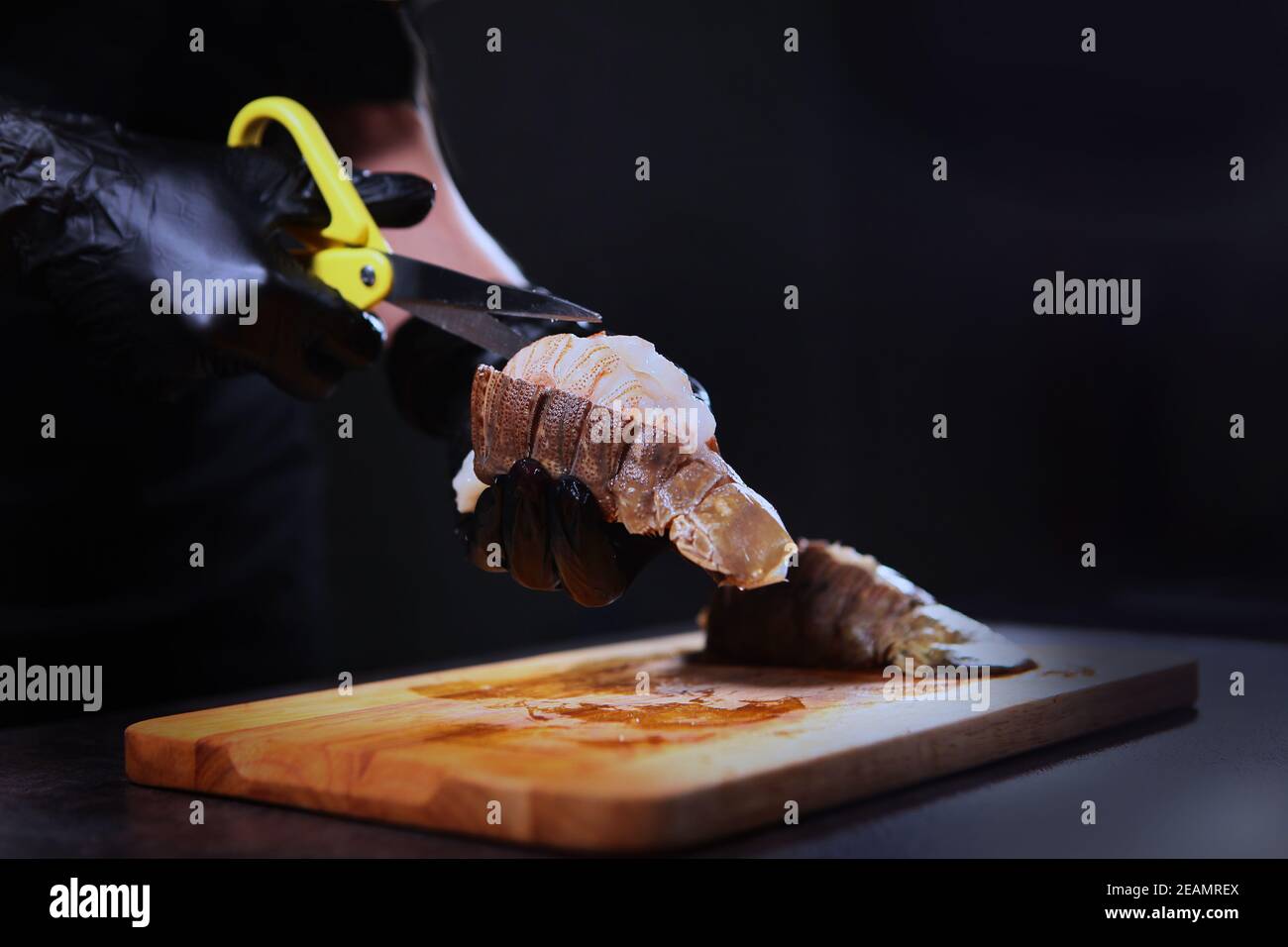 Il cuoco taglia il guscio dell'aragosta con le forbici. Cucina di pesce. Cibo proteico. Persona irriconoscibile. Mani in guanti protettivi. Foto Stock