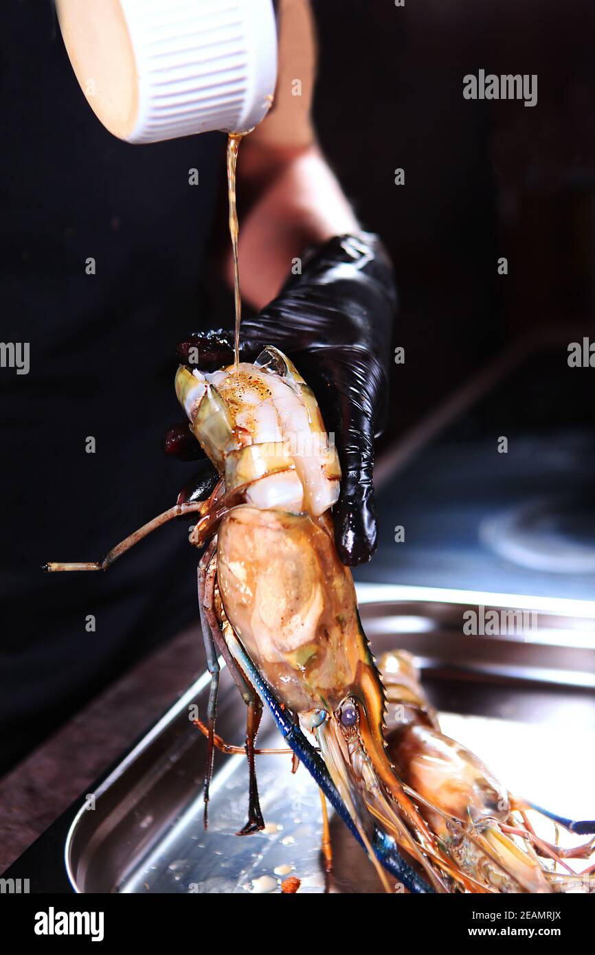 Il cuoco versa la salsa su enormi gamberi d'acqua dolce. Gamberi alla griglia. Foto su sfondo nero. Foto verticale. Concetto di cucina. Foto Stock