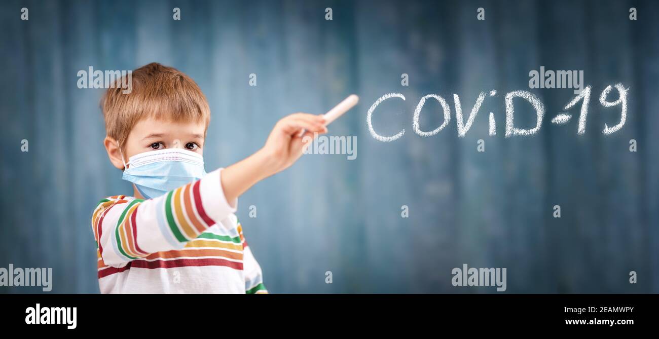 Ragazzo in maschera medica di protezione del viso in interni su sfondo blu. Foto Stock
