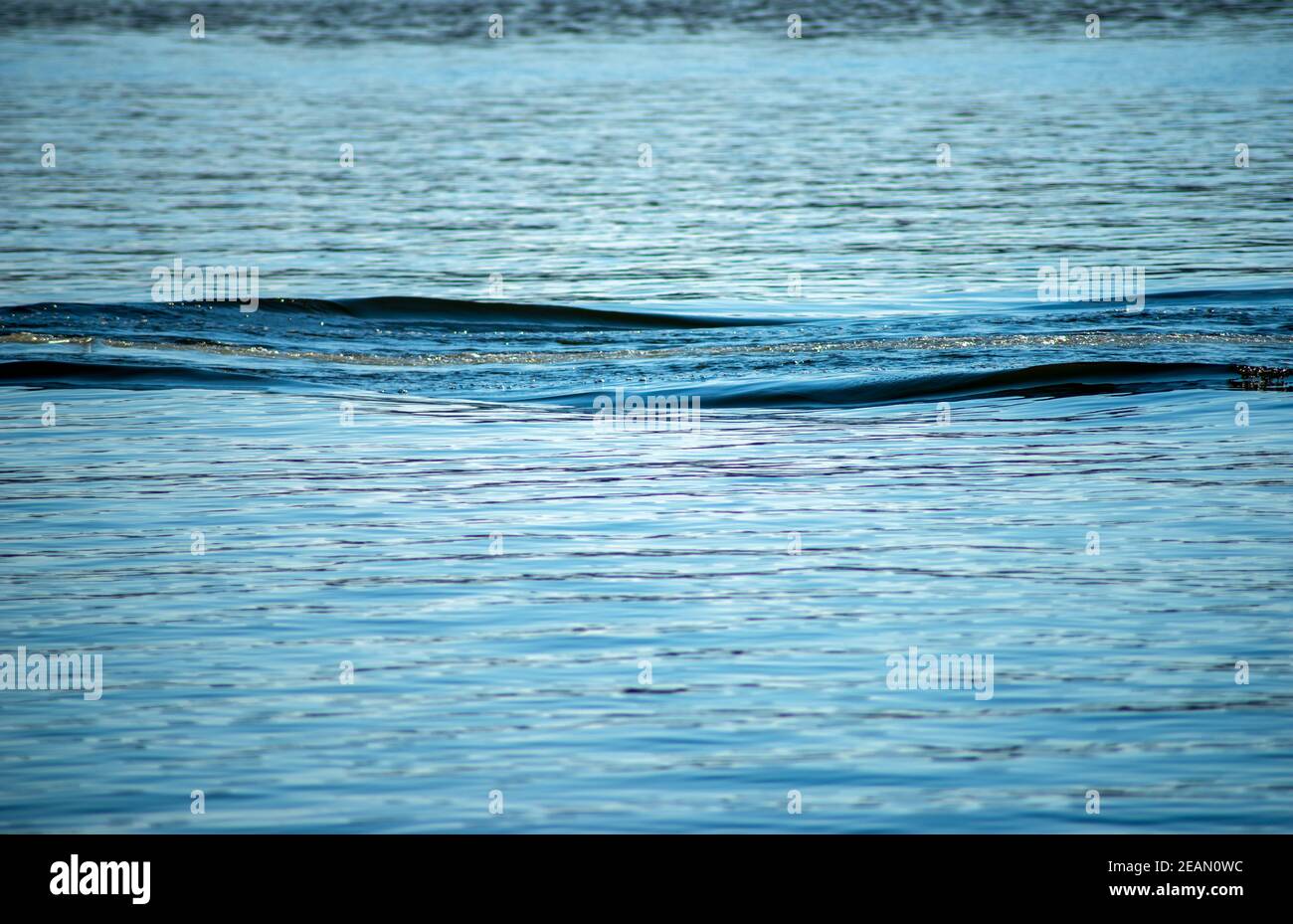 Il risveglio increspa striature su una tranquilla superficie blu dell'acqua Foto Stock