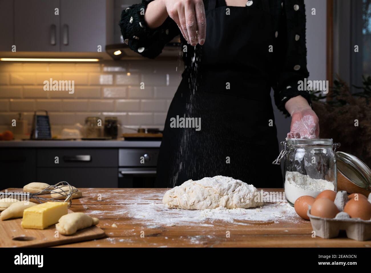 Giovane bella donna impastare impasto ad un tavolo di legno in cucina. Hobby casalinga concetto. Foto Stock