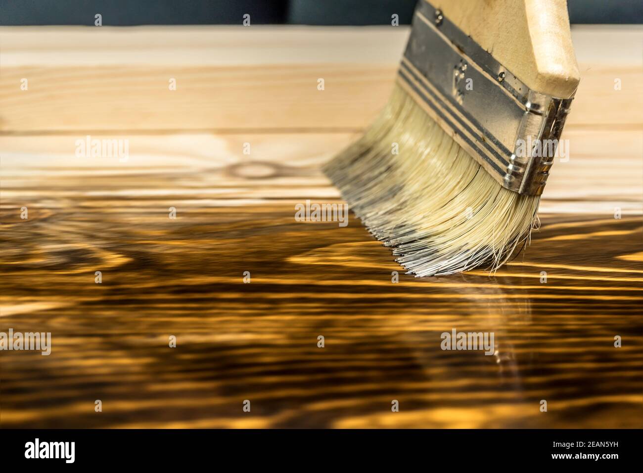 Un primo piano pennello che dipinge un tavolo di legno con macchia o vernice marrone, con l'aspetto della tessitura del legno. Legno, tavole da pittura. Foto Stock