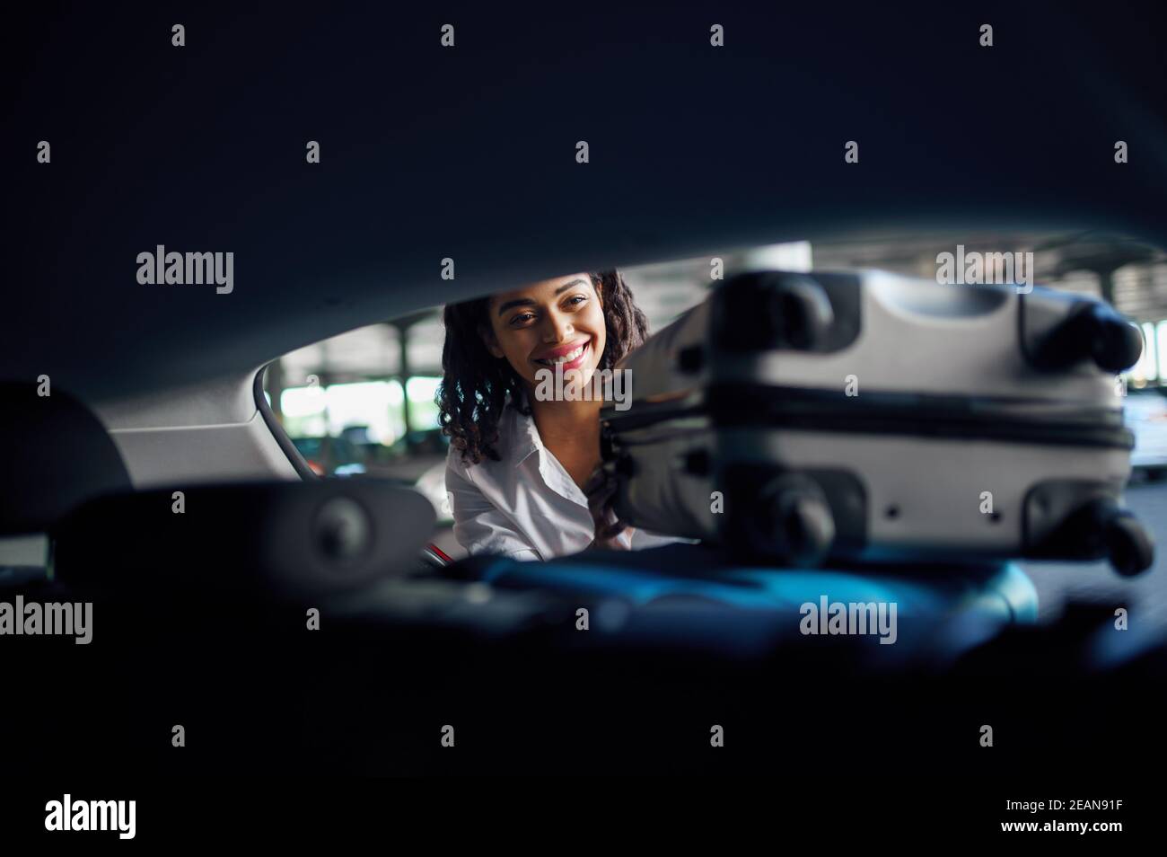 Donna sorridente mette valigie in macchina, parcheggio Foto Stock