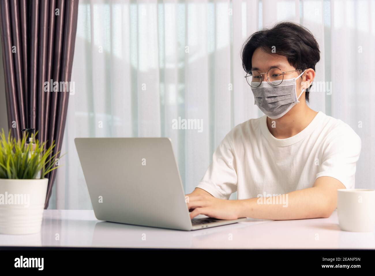 giovane uomo che indossa una maschera protettiva con gel disinfettante accanto lavora da casa Foto Stock