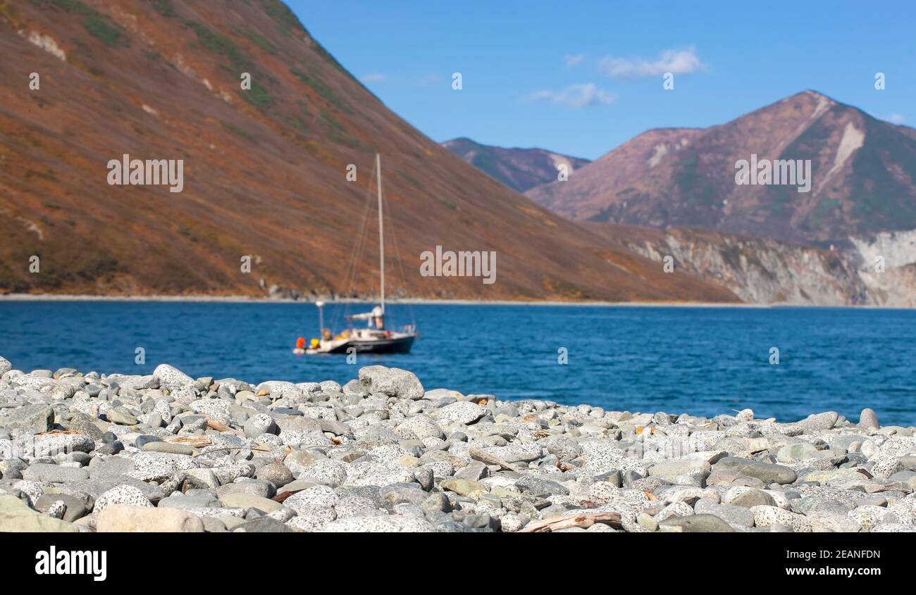 Messa a fuoco selettiva. Spiaggia di ciottoli nella baia settentrionale dell'oceano Pacifico con una barca all'ancora Foto Stock