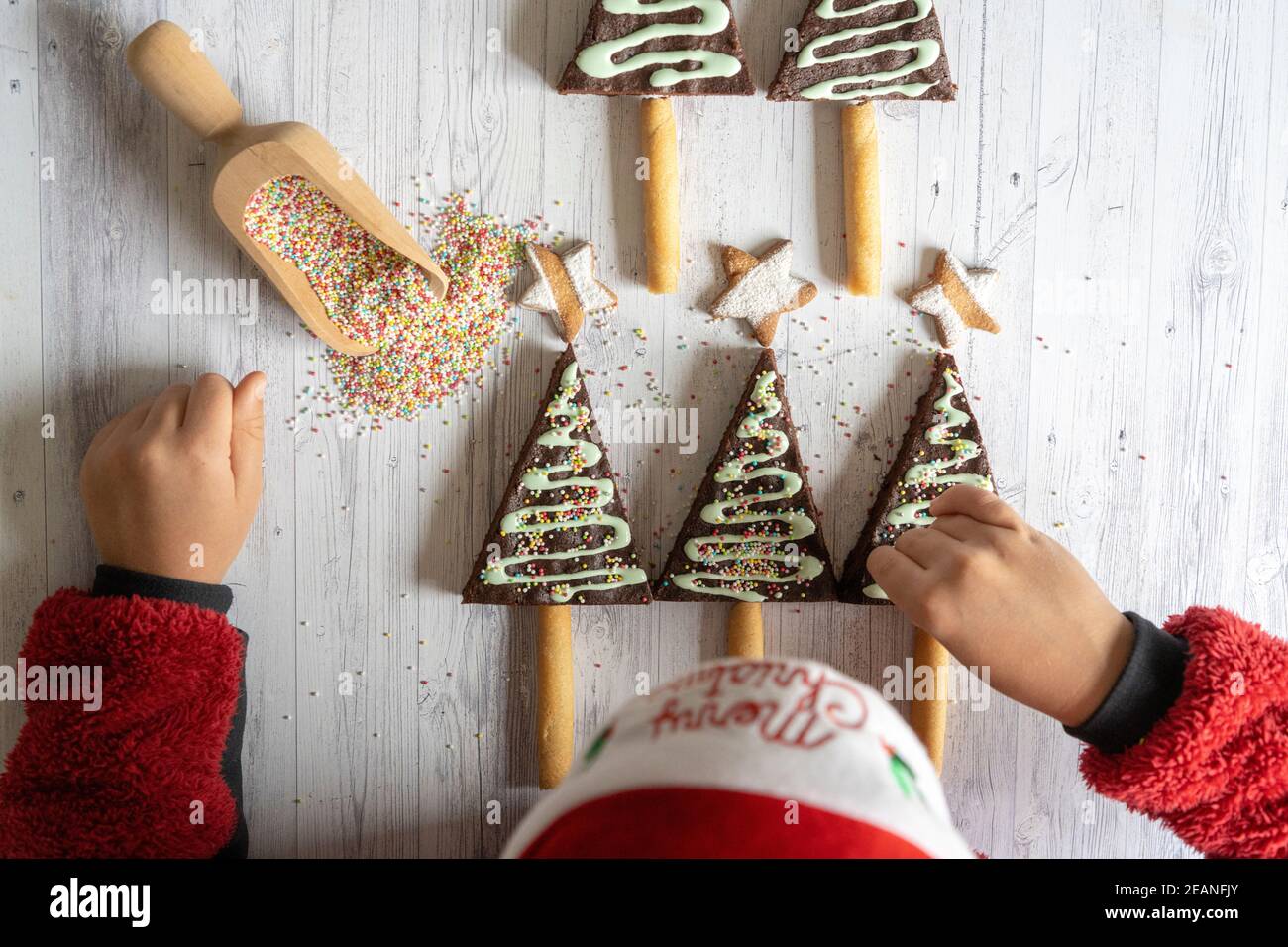 Vista aerea del bambino piccolo con cappello di Santa che decorano i brownie di cioccolato fatti in casa e biscotti a forma di albero di Natale, Italia, Europa Foto Stock