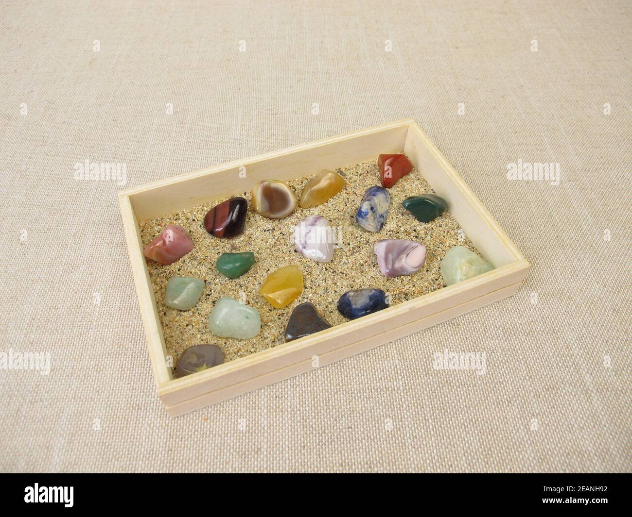 Gemme tumbled in una scatola di legno con sabbia Foto Stock