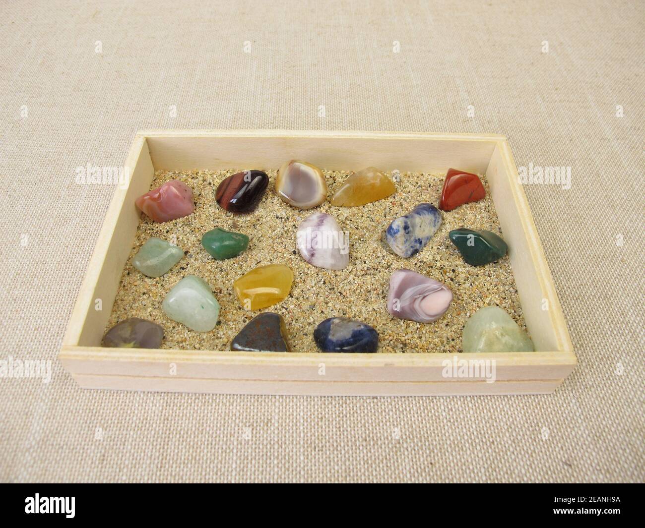 Gemme tumbled in una scatola di legno con sabbia Foto Stock