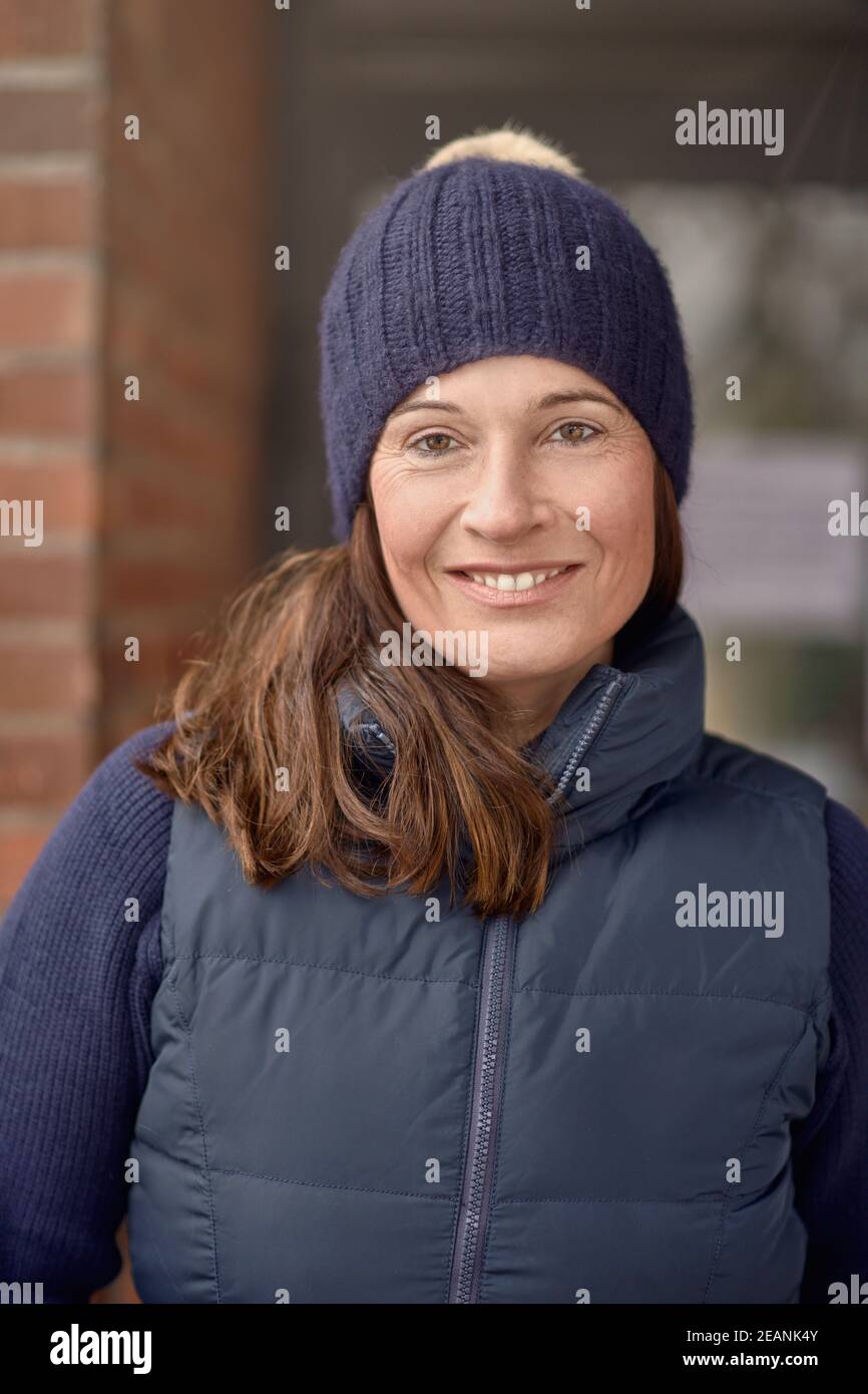 Bella donna sorridente amichevole in outfit inverno blu con maglia cappello e giacca calda in una testa ravvicinata e spalle ritratto esterno Foto Stock
