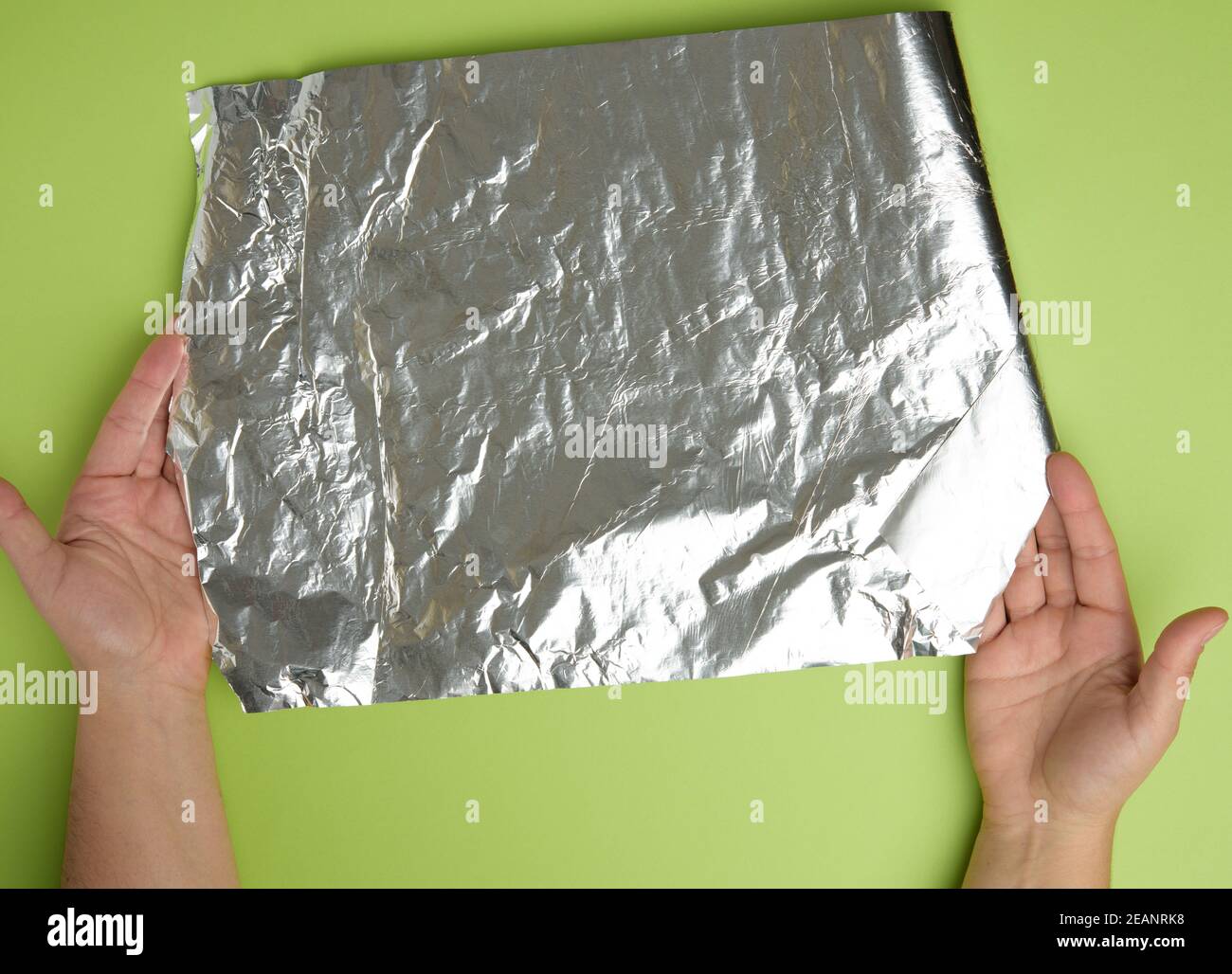 le mani femminili trattengono una lamina d'argento sminuzzata su sfondo verde Foto Stock