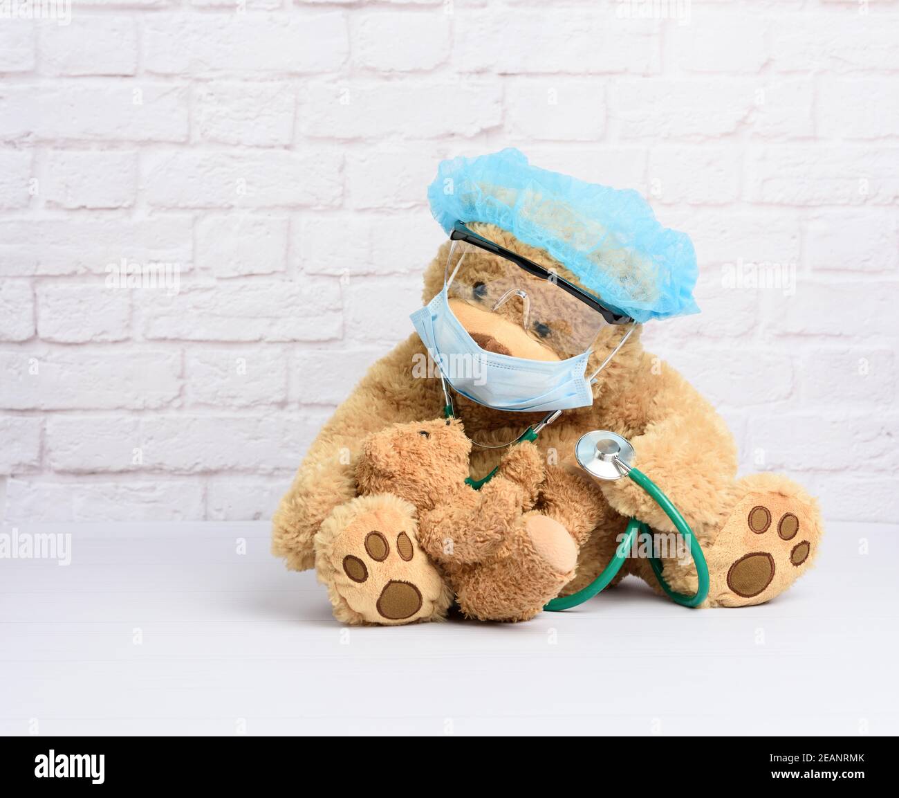 l'orsacchiotto marrone si trova in occhiali protettivi di plastica, una maschera medica monouso e un cappuccio blu Foto Stock