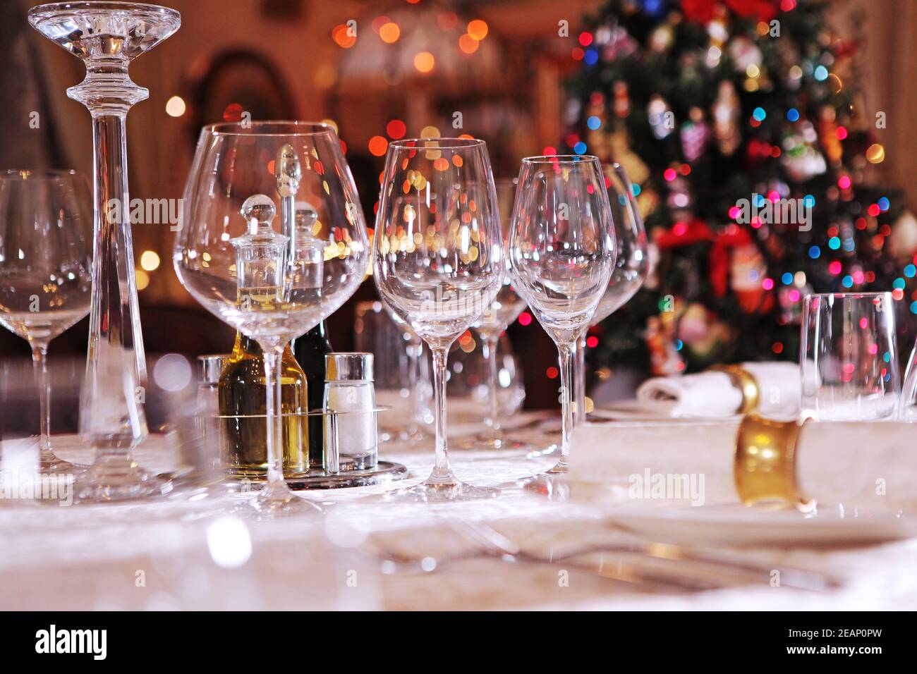 Impostazione del tavolo per le vacanze Capodanno o Natale. Albero di Natale fuori fuoco. Bicchieri di vino in vetro vuoti. Foto Stock