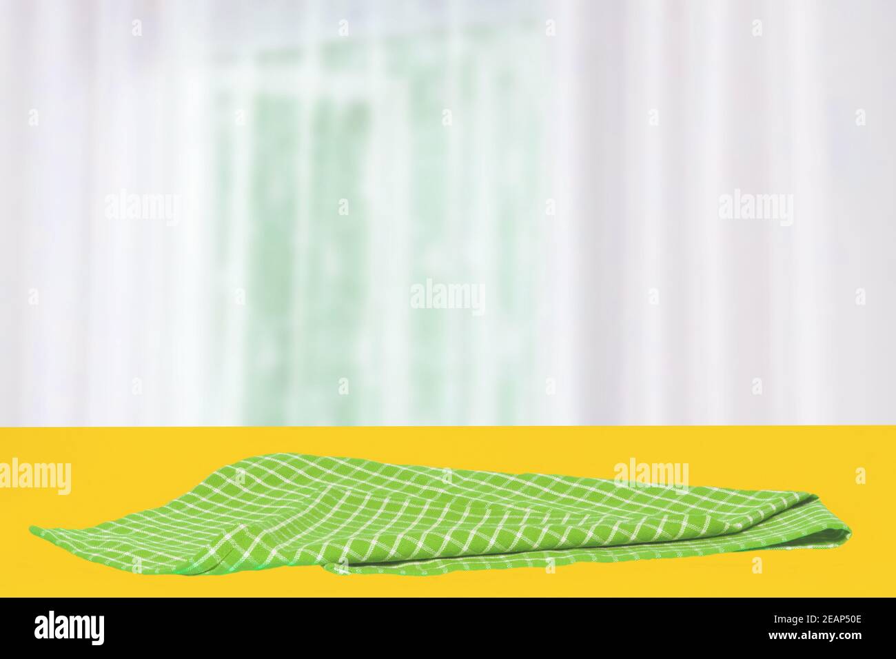 Prodotto da tavolo vuoto. Closeup di un tovagliolo o tovagliolo a scacchi verdi vuoto su un tavolo giallo su uno sfondo astratto della tenda sfocato. Modello per il montaggio dell'esposizione di prodotti e alimenti. Foto Stock