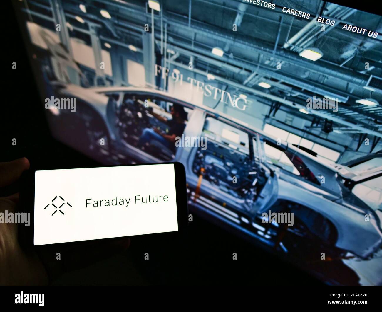 Persona che detiene smartphone con il logo della società americana di veicoli elettrici Faraday Future Inc. Di fronte al sito web. Mettere a fuoco il display del telefono. Foto Stock